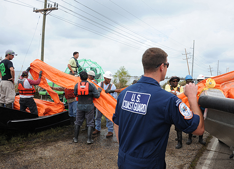 A man in a U.S. Coast Guard uniform directing a line of people moving pollution boom.
