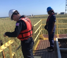 Two people standing on a metal platform looking out at a marsh area.