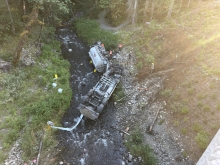 A fuel truck overturned in a Washington creek with responders standing nearby.