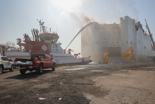 Fire boat spraying water on a large disabled vessel on fire.