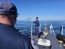 Two U.S. Coast Guard pilots on a vessel retrieve an uncrewed aircraft system.