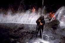 Cleanup workers and hoses spraying out water working to clean off black rocks on a shoreline.
