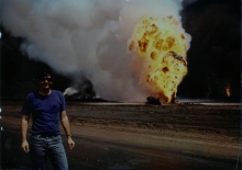 A man standing in front of a fire and a plume of smoke.