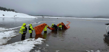 A group of responders deploying a spill boom in a snowy lake to contain an oil spill.