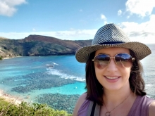 A person posing for a photo with a body of water and mountains in the backgorund.
