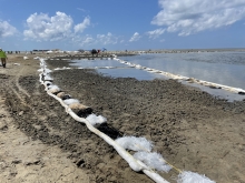 Containment boom are in place to collect oil mobilized by the mechanical tilling of heavily oiled sand from a sandy coastline.
