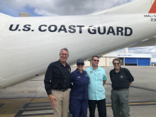 Four individuals supporting hurricane response pose for a group photo in front of an overflight plane.