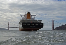 A view of the back of a container ship with a bridge in the background. 
