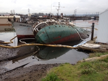 An overturned vessel next to another vessel with pollution boom around it.