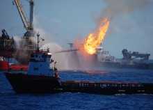 Several boats pump pressurized water onto a fire on a platform. 