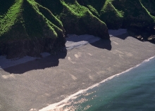 Gravel shoreline with green mountains in the background. 