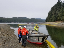 Three people standing near a boat with pollution boom on a body of water in the background.