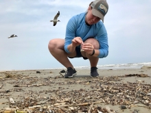 A woman bends down on a beach to put small plastics items into a plastic bag.