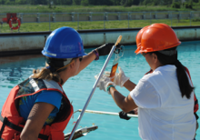 Two people in hard hats looking at a small item on the end of a long pole. 