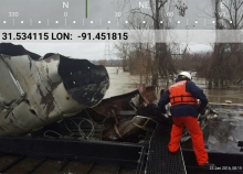 A man standing before a pile of wreckage on a river.