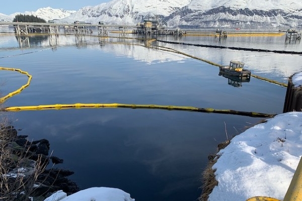Pollution boom around a spot of oil with a snowy mountain range in the background.