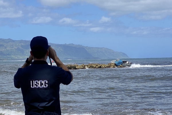 A man in a Coast Guard uniform looking at a wrecked vessel. 