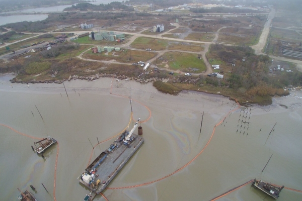 An aerial view of a ship with visible oil sheen and pollution boom around it. 